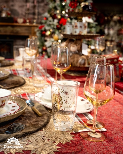 Table décorée dans un style Country Christmas avec verre doré et sapin en arrière-plan.